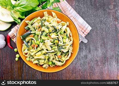 Tagliatelle pasta with zucchini, green peas, asparagus beans, hot pepper and spinach in a plate on napkin, garlic, fork and basil on wooden board background from above