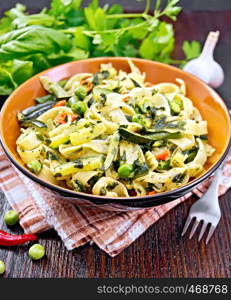 Tagliatelle pasta with zucchini, green peas, asparagus beans, hot pepper and spinach in a plate on napkin, garlic, fork and basil on wooden board background