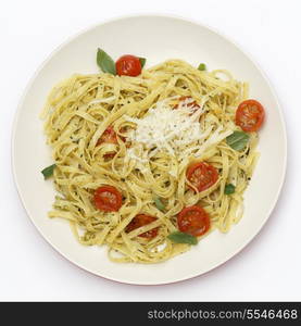 Tagliatelle ribbon pasta tossed with a green, basil pesto and grilled cherry tomatoes, garnished with basil leaves, topped with fresh-grated parmesan, viewed from above. A simple but tasty Italian-style lunch.