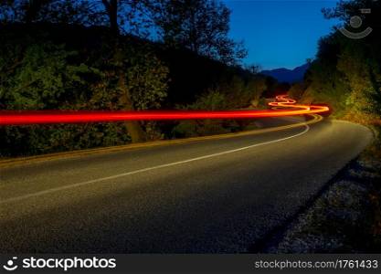 Taillights illuminate an empty road in a summer night forest. Long winding trails. Taillight Trails on the Night Road