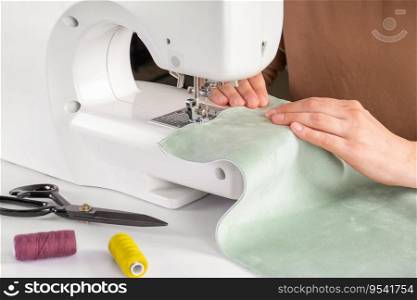 Tailor hands stitching green fabric on modern sewing machine at workplace in atelier. Women’s hands sew pieces of fabric on sewing machine closeup. Handmade, hobby, repair, small business concept