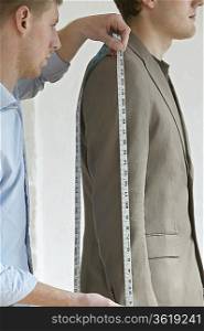 Tailor measuring jacket sleeve on man, side view, close up