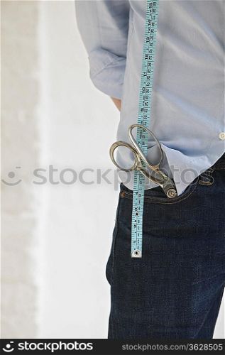 Tailor with scissors in pocket and measuring tape, standing indoors, mid section, close up