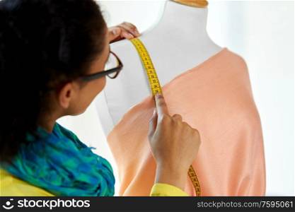 tailoring, sewing and clothing concept - close up of african american fashion designer measuring dress with tape measure. fashion designer measuring dress with tape measure