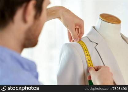 tailoring, sewing and clothing concept - close up of male fashion designer measures jacket with tape measure. fashion designer measures jacket with tape measure