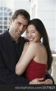 Taiwanese mid adult woman and Caucasian man outdoors embracing and smiling at viewer.