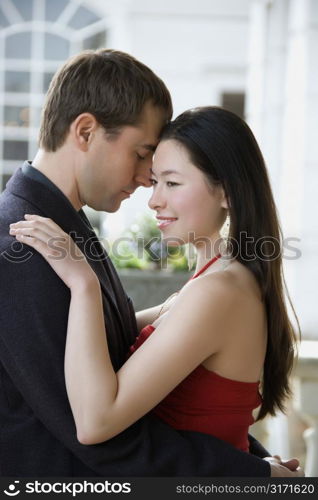 Taiwanese mid adult woman and Caucasian man outdoors embracing each other.