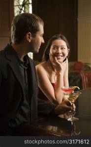 Taiwanese mid adult woman and Caucasian man standing at bar with drinks.