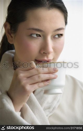 Taiwanese mid adult woman in bathrobe drinking coffee and looking to side.