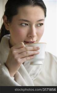 Taiwanese mid adult woman in bathrobe drinking coffee and looking to side.