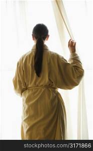 Taiwanese mid adult woman in bathrobe looking out window.