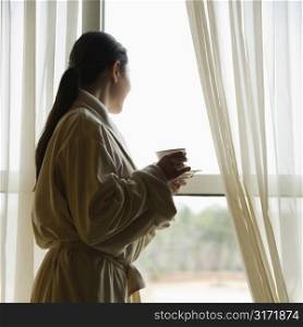 Taiwanese mid adult woman in bathrobe looking out window.