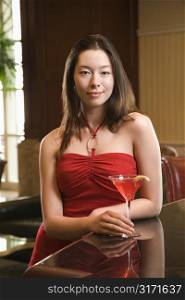 Taiwanese mid adult woman in red dress at bar with a drink.