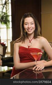 Taiwanese mid adult woman in red dress smiling and standing at bar with drink.