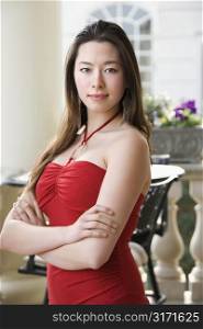 Taiwanese mid adult woman in red dress with arms crossed looking at viewer.