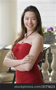 Taiwanese mid adult woman in red dress with arms crossed smiling at viewer.