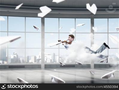 Take a break and relax. Young businessman flying in modern office and playing violin