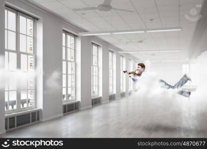 Take a break and relax. Young businessman flying in modern office and playing violin