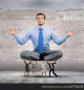 Take a break. Young meditating businessman supported by business colleagues