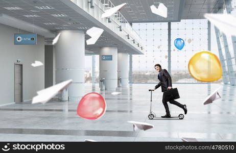 Take a five minute break. Young cheerful businessman in suit riding scooter in office