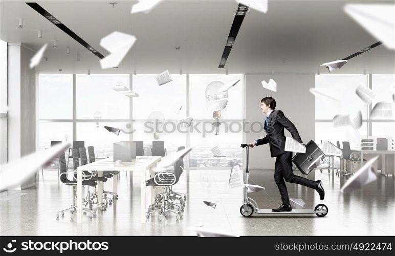 Take a five minute break. Young cheerful businessman in suit riding scooter in office