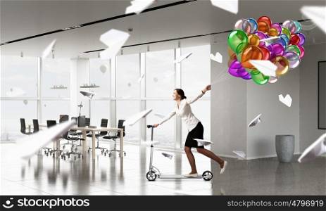 Take a five minute break. Young cheerful businesswoman in suit riding scooter in office
