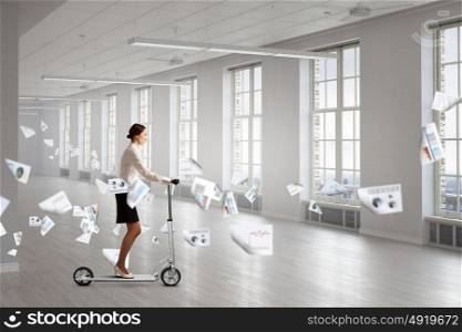 Take a five minute break. Young cheerful businesswoman in suit riding scooter in office