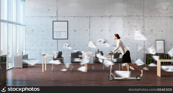 Take a five minute break. Young cheerful businesswoman in suit riding scooter in office