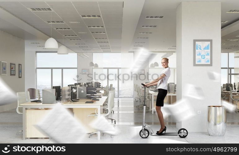 Take a five minute break. Young cheerful businesswoman in suit riding scooter in office