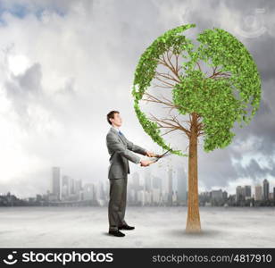 Take care of our home. Young businessman cutting tree with scissors in shape of Earth planet