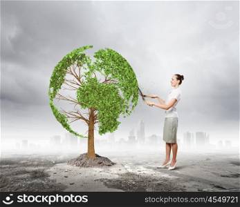 Take care of our home. Young businesswoman cutting tree with scissors in shape of Earth planet
