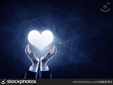 Take care of your heart. Businessman hands on dark background holding with care digital heart