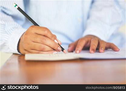 take the exam final high school university student holding pencil writing on paper answer sheet / education college in class taking notes sitting learning writing selected choice in examination room
