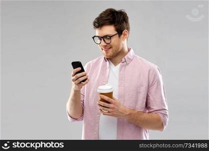 takeaway and people concept - young man or student in glasses with smartphone drinking coffee over grey background. man in glasses with smartphone drinking coffee