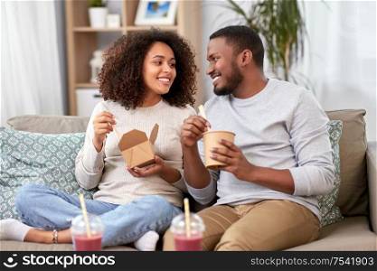 takeaway food, drinks and people concept - happy african american couple eating wok with chopsticks at home. happy couple with takeaway food and drinks at home