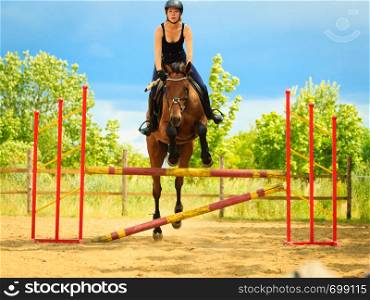 Taking care of animals, horsemanship, western competitions concept. Jockey young girl doing horse jumping through hurdle on sunny day. Jockey young girl doing horse jumping through hurdle