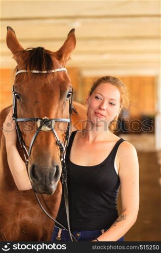 Taking care of animals, love and friendship concept. Jockey young girl petting and hugging brown horse in stable. Jockey young girl petting and hugging brown horse