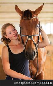 Taking care of animals, love and friendship concept. Jockey young girl petting and hugging brown horse in stable. Jockey young girl petting and hugging brown horse