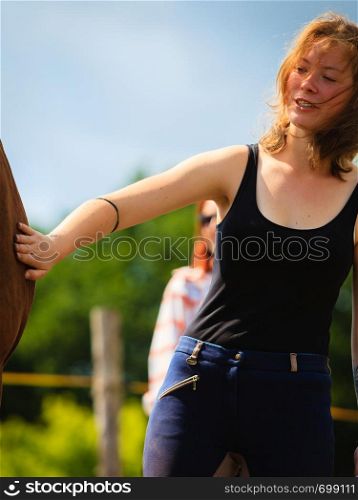 Taking care of animals, love and friendship concept. Jockey young girl petting brown horse on sunny day. Jockey young girl petting brown horse
