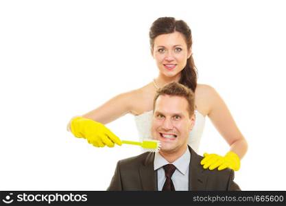 Taking care of house together, sharing household duties concept. Bride in wedding dress and groom wearing elegant suit holding cleaning equipment and tools.. Bride and groom sharing household duties