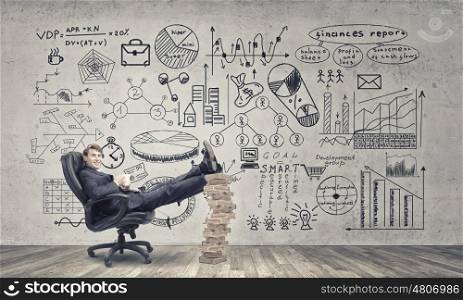 Taking coffee break. Young handsome businessman sitting in chair with his legs on pile of books