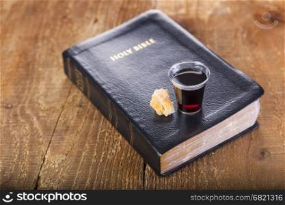 Taking Communion. Cup of glass with red wine, bread and Holy Bible on wooden table close-up. Focus on glass