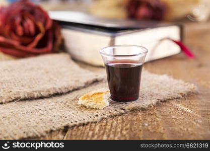 Taking Communion. Cup of glass with red wine, bread and Holy Bible on wooden table close-up. Focus on bread