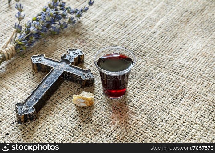 Taking communion with glass of wine and bread near cross and lavanda on the textile tablecloth. 