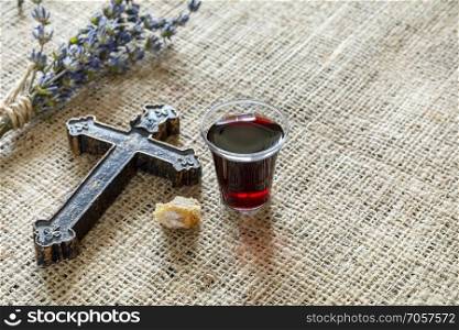 Taking communion with glass of wine and bread near cross and lavanda on the textile tablecloth. 