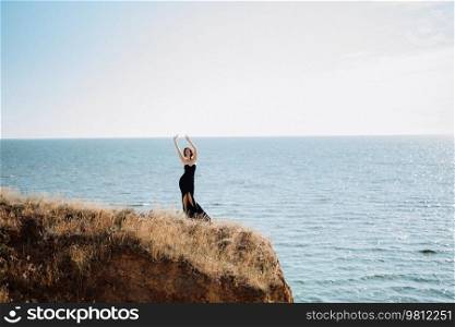 tall girl model in a black dress on the mountain hills near the sea