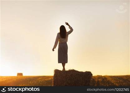tall girl stands on a haystack in a field at sunset.. tall girl stands on a haystack in a field at sunset