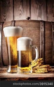 Tall glass and a mug of light beer on a background of the old wooden barrels. Tall glass and a mug of light beer