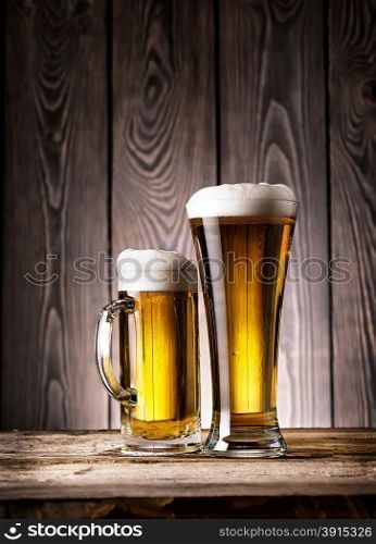 Tall glass and mug of light beer with foam on wooden background. Tall glass and mug of light beer with foam