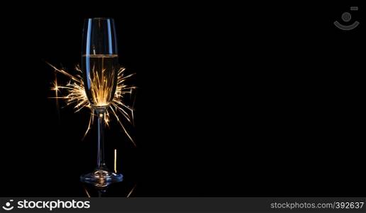 Tall glass of champagne with Bengal lights. Black background. The concept of the celebration of the wedding and the new year. Copy space.. Tall glass of champagne with Bengal lights